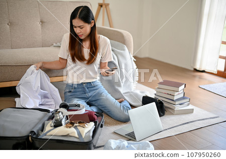 A busy Asian woman is preparing her belongings and packing her luggage in her living room A busy Asian woman is preparing her belongings and packing her luggage in her living room 107950260