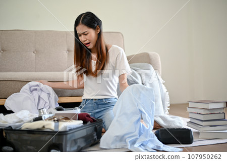 An unhappy Asian woman feels stressed about her overfilled of clothes while packing her suitcase 107950262