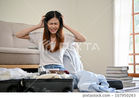 A furious Asian woman feels stressed about her overfilled of stuff while packing her suitcase 107950263