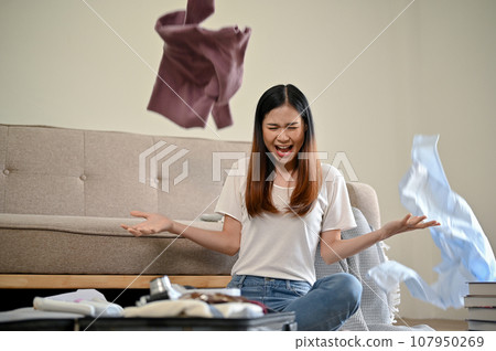 A crazy Asian girl throws her clothes up in the air while packing her suitcase at home. A crazy Asian girl throws her clothes up in the air while packing her suitcase at home. 107950269