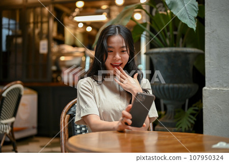 An excited Asian woman is looking at her smartphone screen with a surprising face An excited Asian woman is looking at her smartphone screen with a surprising face 107950324