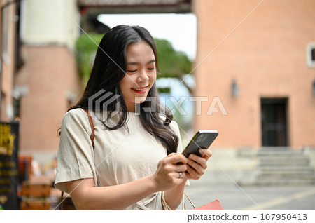 An attractive Asian woman using her smartphone while shopping at the city square An attractive Asian woman using her smartphone while shopping at the city square 107950413