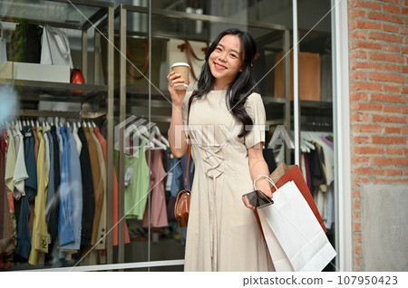 An attractive Asian girl enjoys her shopping day alone in the city, carrying her shopping bags An attractive Asian girl enjoys her shopping day alone in the city, carrying her shopping bags 107950423