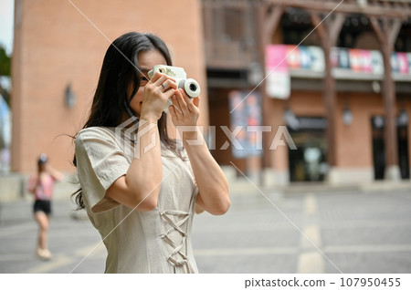 A beautiful Asian female tourist strolling around, shooting cityscapes with her instant camera. A beautiful Asian female tourist strolling around, shooting cityscapes with her instant camera. 107950455