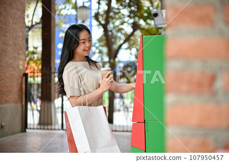 A beautiful Asian woman withdraws her money from an ATM on the shopping street A beautiful Asian woman withdraws her money from an ATM on the shopping street 107950457