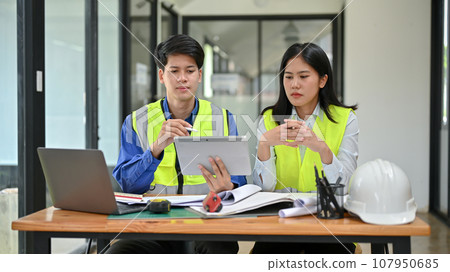 Two professional and serious Asian engineers are discussing work, and working on a project together. Two professional and serious Asian engineers are discussing work, and working on a project together. 107950685