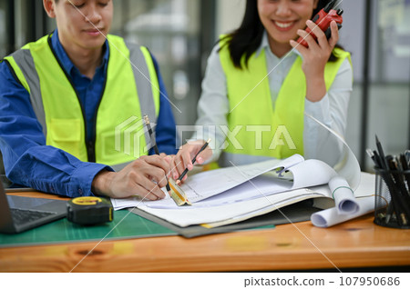 Two professional Asian construction engineers are checking a blueprint, discussing work Two professional Asian construction engineers are checking a blueprint, discussing work 107950686