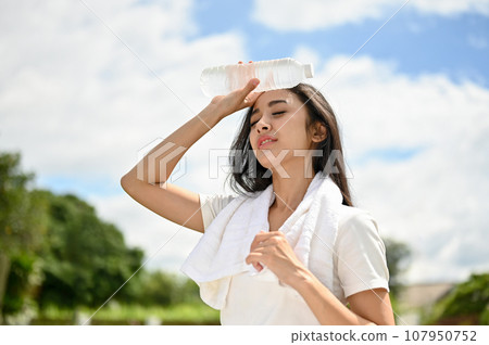 An exhausted and sweaty Asian woman feeling hot and tired, rests after a long run at the park An exhausted and sweaty Asian woman feeling hot and tired, rests after a long run at the park 107950752