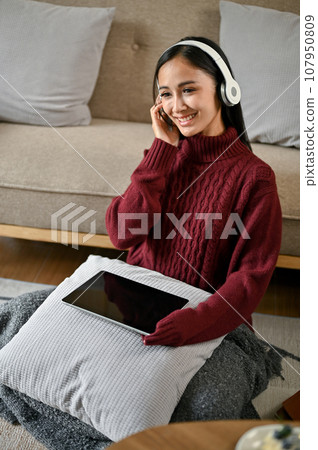 A woman enjoys listening to music while relaxing in her living room on a winter day. A woman enjoys listening to music while relaxing in her living room on a winter day. 107950809