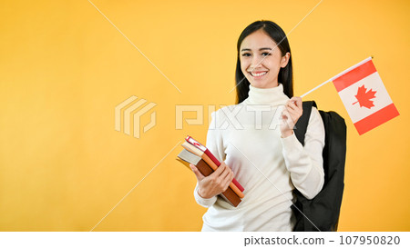 A pretty Asian female college student is holding her books and the Canada flag. Exchange student A pretty Asian female college student is holding her books and the Canada flag. Exchange student 107950820