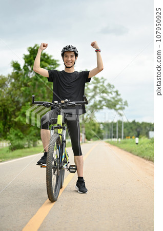 A happy Asian man raises his hands on his bike, ready to bike or achieve his cycling goal. 107950925