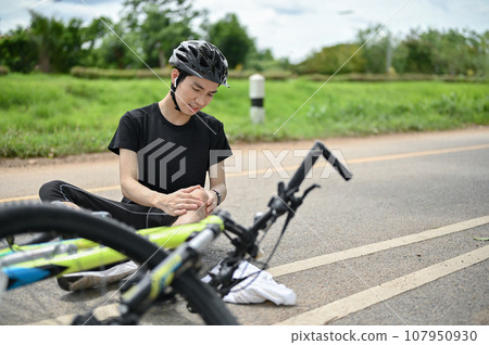 An injured young Asian male cyclist fell off the bike while biking along country roads An injured young Asian male cyclist fell off the bike while biking along country roads 107950930