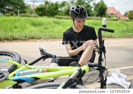 An injured young Asian male cyclist in sportswear and a bike helmet fell off the bike An injured young Asian male cyclist in sportswear and a bike helmet fell off the bike 107950934