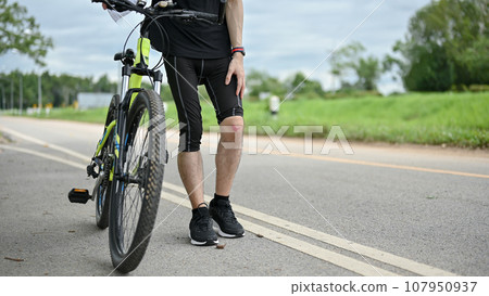 Cropped image of an injured male cyclist walking along the street with his bike Cropped image of an injured male cyclist walking along the street with his bike 107950937