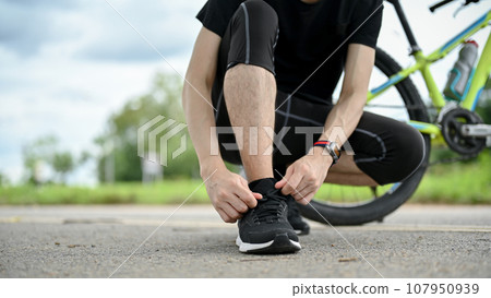 Cropped image of a healthy, fit male cyclist tying his shoelaces before riding a bike Cropped image of a healthy, fit male cyclist tying his shoelaces before riding a bike 107950939