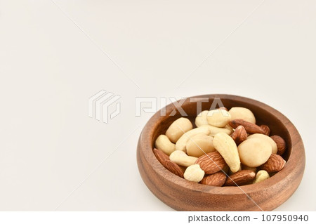 Unglazed mixed nuts on a wooden plate 107950940