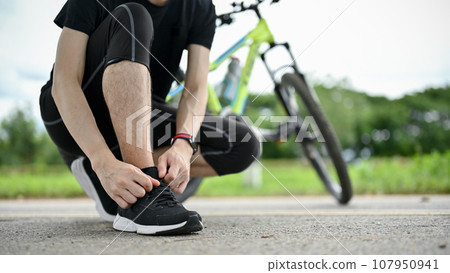 A male cyclist tying his shoelaces before riding a bike on the country roads. 107950941