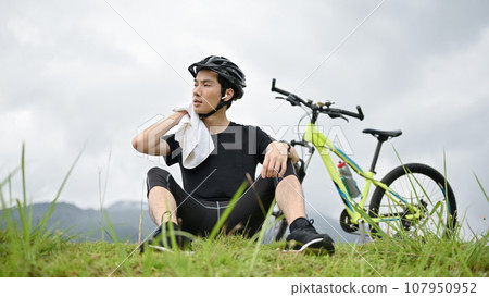 A tired young Asian man rests on the grass after a long bike ride in the mountains. A tired young Asian man rests on the grass after a long bike ride in the mountains. 107950952