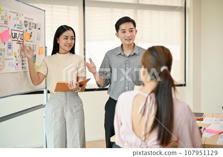 Two Asian tech developers are presenting their new project to their team in the meeting. Two Asian tech developers are presenting their new project to their team in the meeting. 107951129