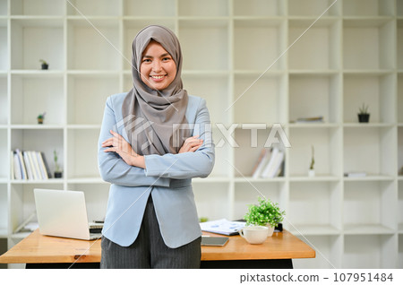 A beautiful Muslim businesswoman stands in the office with her arms crossed. A beautiful Muslim businesswoman stands in the office with her arms crossed. 107951484