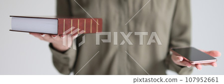 Confused woman holds book and smartphone making choice Confused woman holds book and smartphone making choice 107952661