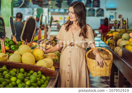 A glowing pregnant woman after forty makes a healthy choice as she selects organic vegetables and fruits at the vibrant organic market, prioritizing her well-being and her baby's health 107952919