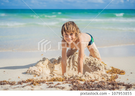 Young boy's pure delight as he explores the sandy playground of the beach, shaping dreams with grains of sand 107953855