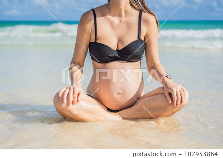 Expectant mother finds inner calm through meditation by the tranquil turquoise sea. A serene moment of pregnancy and peace 107953864