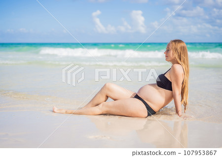 Radiant pregnant woman in a swimsuit, amid the stunning backdrop of a turquoise sea. Serene beauty of maternity by the shore Radiant pregnant woman in a swimsuit, amid the stunning backdrop of a turquoise sea. Serene beauty of maternity by the shore 107953867