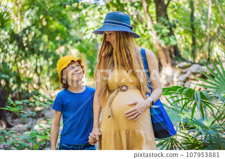 Expectant mother and her son enjoying a leisurely stroll in the park, cherishing precious moments amidst nature's beauty Expectant mother and her son enjoying a leisurely stroll in the park, cherishing precious moments amidst nature's beauty 107953881