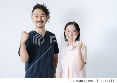 Men and women in white coats, doctors and nurses, fist pump while looking at the camera Men and women in white coats, doctors and nurses, fist pump while looking at the camera 107954411