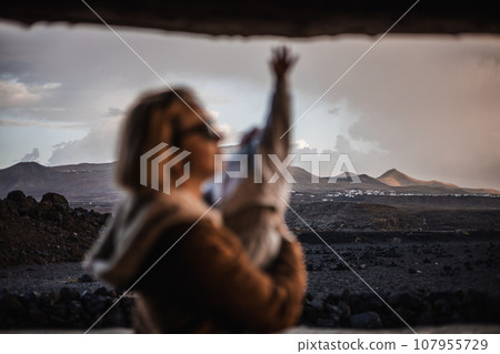Mother enjoying winter vacations playing with his infant baby boy son on black sandy volcanic beach of Janubio on Lanzarote island, Spain on windy overcast day. Family travel vacations concept 107955729