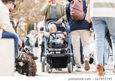 Mother walking and pushing his infant baby boy child in stroller in crowd of people wisiting sunday flea market in Malaga, Spain 107955745