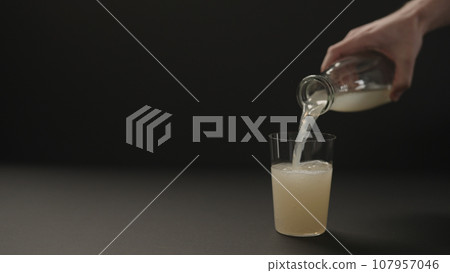 man hand pour lemon ginger lemonade into tumbler glass on black paper background with copy space 107957046