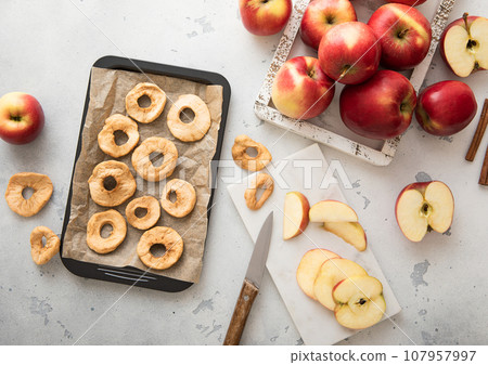 Sweet dried apple rings on baking tray with knife red ripe apples. 107957997