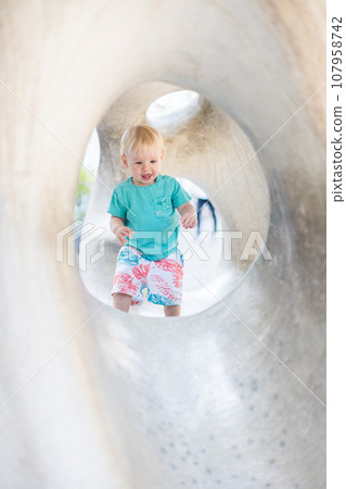 Child playing on outdoor playground. Toddler plays on school or kindergarten yard. Active kid on stone sculpured slide. Healthy summer activity for children. Little boy climbing outdoors 107958742