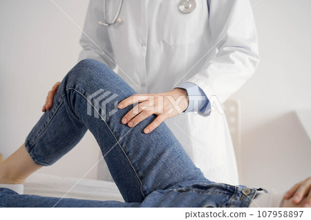 Doctor and patient are at the usual medical inspection in the clinic. Therapist examines a young woman's knee. Medicine concept Doctor and patient are at the usual medical inspection in the clinic. Therapist examines a young woman's knee. Medicine concept 107958897