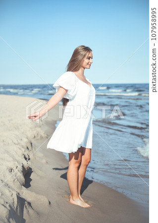 Happy, beautiful woman on the ocean beach standing in a white summer dress, open arms 107958995