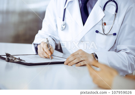 Unknown male doctor and patient woman discussing something while sitting in clinic and using clipboard. Best medical service in hospital, medicine, pandemic stop 107959026