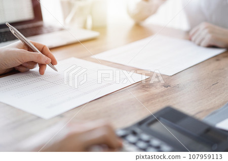 Two accountants using a laptop computer and calculator while counting taxes at wooden desk in office. Teamwork in business audit and finance 107959113