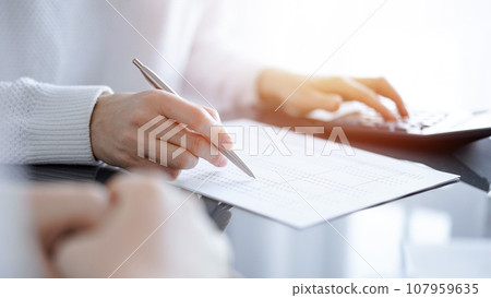 Woman accountant using a calculator and laptop computer while counting taxes for a client. Business audit concepts 107959635