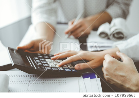 Woman accountant using a calculator and laptop computer while counting taxes for a client. Business audit and finance concepts 107959665