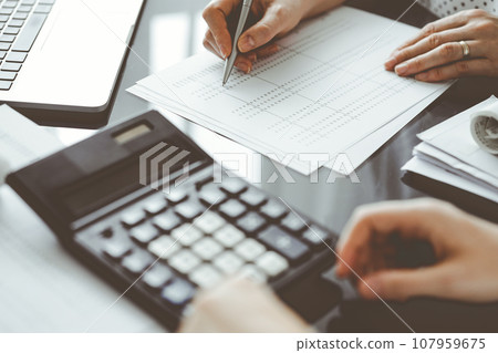Woman accountant using a calculator and laptop computer while counting taxes for a client. Business audit and finance concepts 107959675
