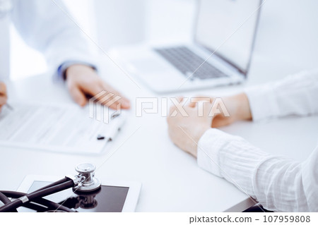 Stethoscope lying on the tablet computer in front of a doctor and patient sitting opposite each other at the background . Medicine, healthcare concept 107959808