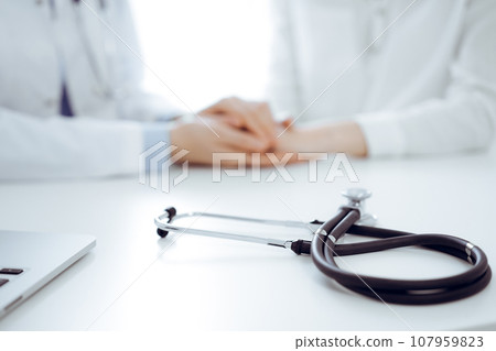 Stethoscope lying on the tablet computer in front of a doctor and patient sitting near each other. Medicine, reassuring hands concept 107959823