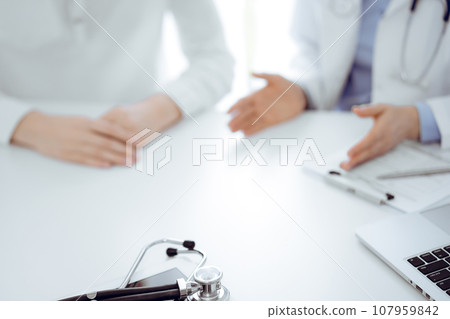 Stethoscope lying on the tablet computer in front of a doctor and patient sitting near of each other at the background. Medicine, healthcare concept 107959842