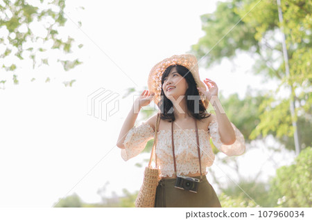 Portrait of asian young woman traveler with weaving hat and basket and a camera on green public park nature background. Journey trip lifestyle, world travel explorer or Asia summer tourism concept. Portrait of asian young woman traveler with weaving hat and basket and a camera on green public park nature background. Journey trip lifestyle, world travel explorer or Asia summer tourism concept. 107960034