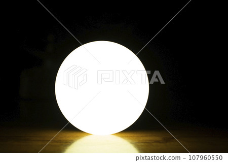 glowing bulb on wooden table in dark room with black background. 107960550