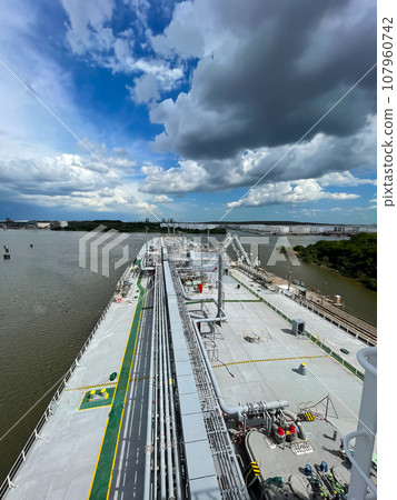 View from the deck of a gas tanker to the seashore, mountains can be seen in the distance. Calm sunny weather, beautiful blue sky with small clouds. View from the deck of a gas tanker to the seashore, mountains can be seen in the distance. Calm sunny weather, beautiful blue sky with small clouds. 107960742