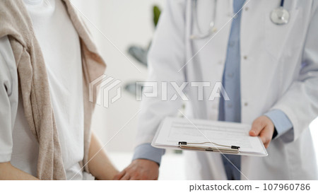 Doctor and patient in clinic. Friendly physician examining a young woman with a one hand while keeping a clipboard with medical records in another. Medicine concept 107960786